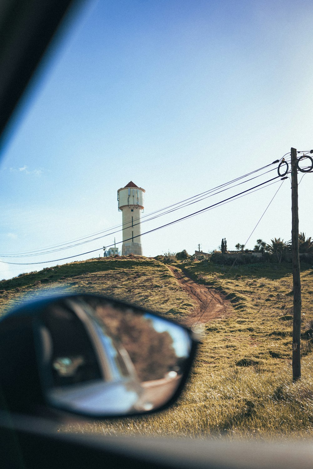 a car's side view mirror shows a light house on a hill