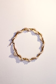 A delicate hoop earring featuring small white pearls evenly spaced along a twisted gold wire. The earring is laid flat against a plain, light-colored background, casting soft shadows.