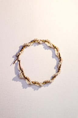 A delicate hoop earring featuring small white pearls evenly spaced along a twisted gold wire. The earring is laid flat against a plain, light-colored background, casting soft shadows.