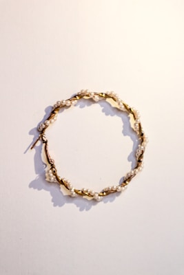 A delicate hoop earring featuring small white pearls evenly spaced along a twisted gold wire. The earring is laid flat against a plain, light-colored background, casting soft shadows.