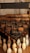 A vintage bowling pin setting machine is hanging above a set of bowling pins. The machine has an industrial look, with metal and wooden components, and includes a sign reading 'Backus Automatic Pin Setter Co. Smethport PA.' The bowling pins are arranged in typical formation and appear aged with some scuff marks.