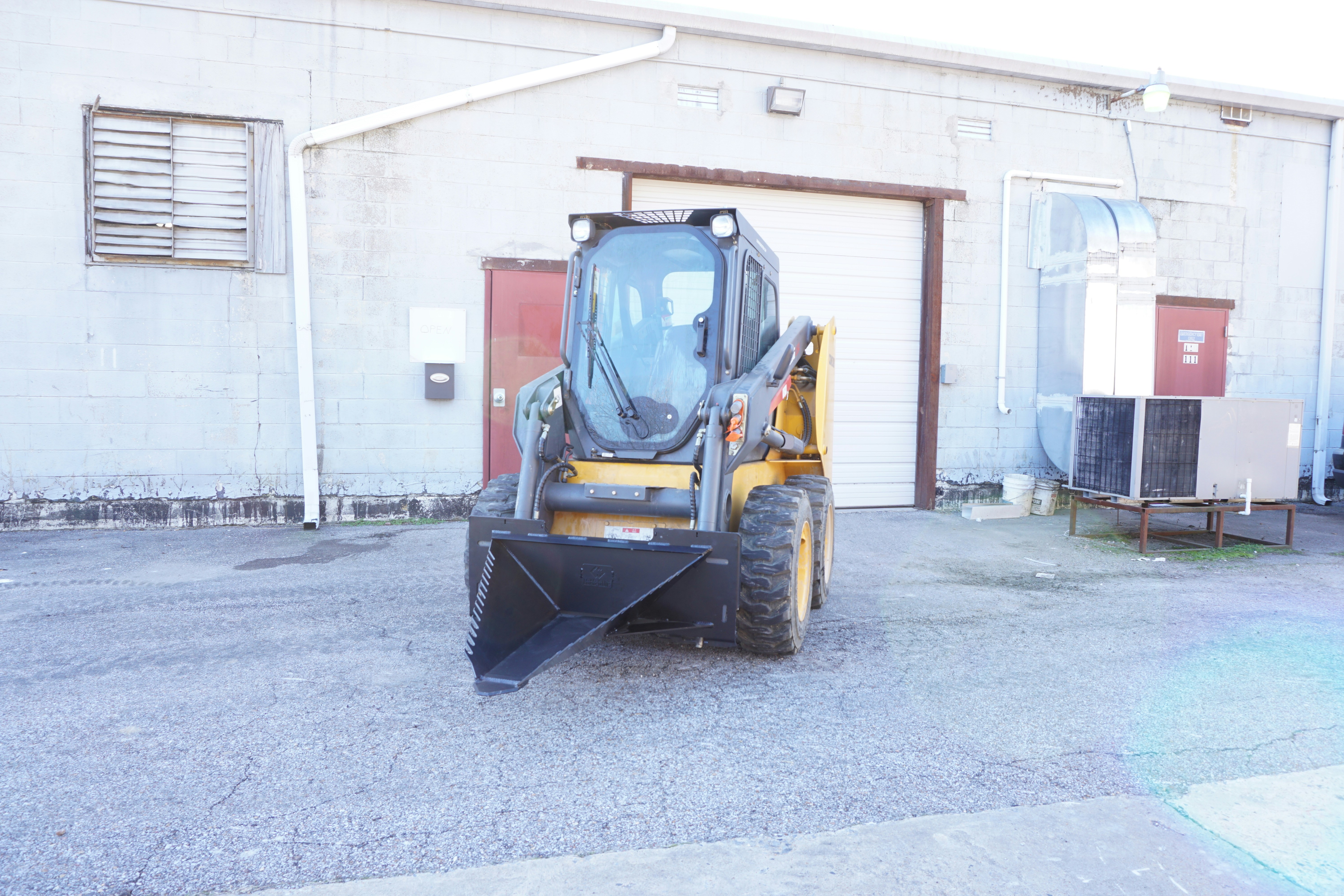 Compact skid steer loader in warehouse yard, small yellow machine with bucket attachment