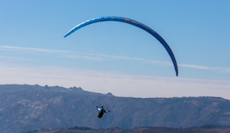 A tandem paraglider soaring above the Cerro Arco with Mendoza city and mountains in the background under a clear blue sky.