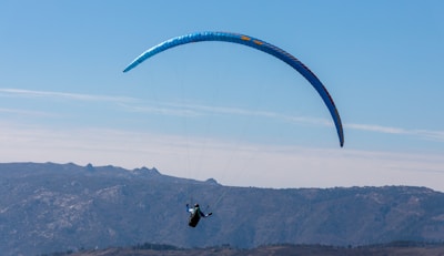 A tandem paraglider soaring above the Cerro Arco with Mendoza city and mountains in the background under a clear blue sky.