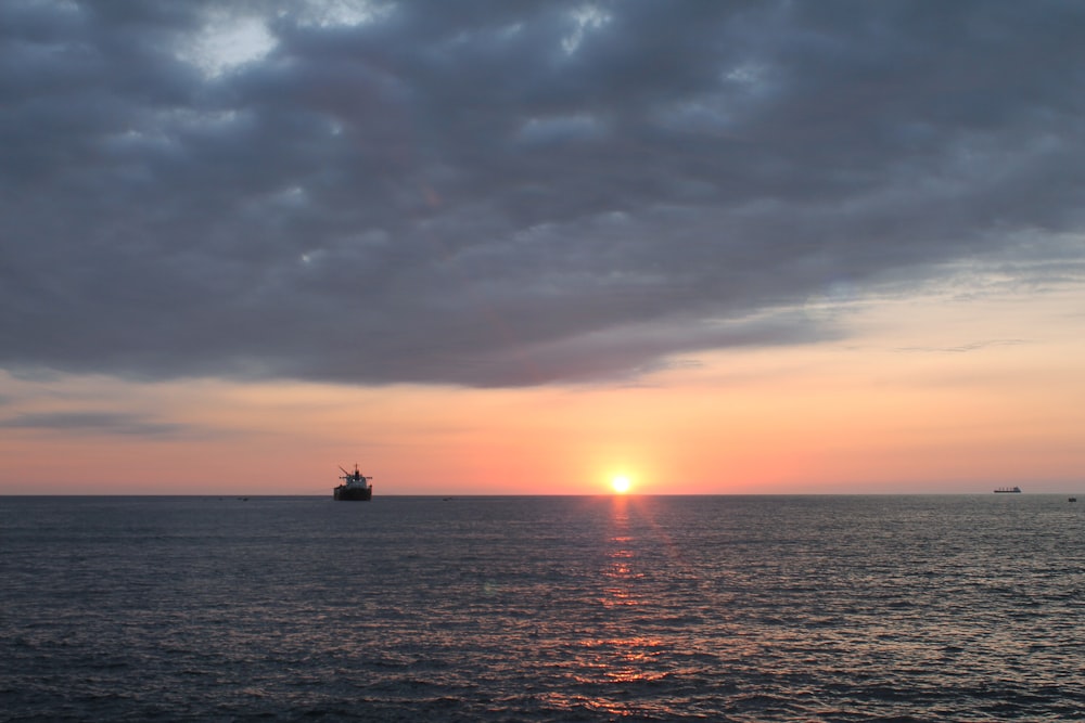 the sun is setting over the ocean with a ship in the distance