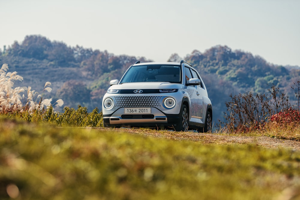 a small white car driving down a dirt road