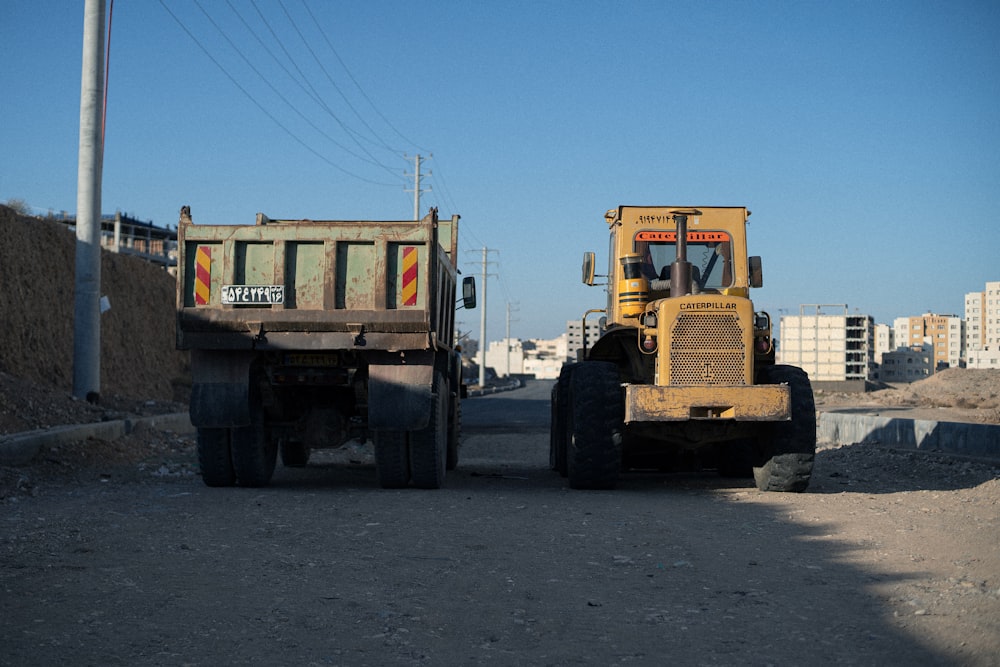 a couple of dump trucks driving down a dirt road