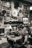 A vintage-themed room decorated with numerous retro signs and memorabilia related to cars, including Ford and Mustang. There is a classic dining booth setup with a table and chairs, a lava lamp, and model cars displayed on a shelf. The walls are adorned with various automotive-themed signs, posters, and a large vintage clock.