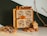 A small wooden cabinet featuring intricately carved drawer fronts is displayed. Cinnamon sticks protrude from the drawers, adding a rustic touch. Nearby, dried orange slices, a decorative miniature house, and a natural branch create an autumnal or holiday atmosphere.