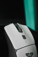 A sleek, modern computer mouse predominantly white with gray accents. It features a scroll wheel and several buttons, indicating a design suitable for gaming or productivity. The mouse is positioned against a dark background with a teal vertical light strip.
