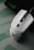 A sleek white gaming mouse with a modern design rests on a subtle green and grey patterned surface. The mouse features a scroll wheel and a logo on its surface.