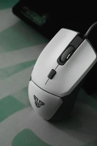 A high-precision gaming mouse resting on a textured mousepad with subtle green and red accents.