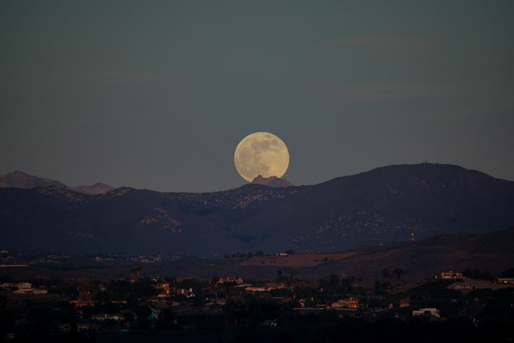 a full moon rising over a mountain range