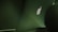 An image featuring the back of an open laptop displaying the illuminated logo. The laptop sits on a table in a dimly lit environment, with the scene predominantly bathed in shades of green.