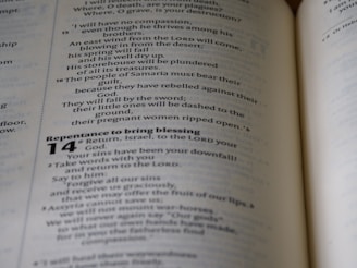 An open book showing text printed in a column format, with headings and verse numbers. The visible page contains religious or biblical content with passages discussing themes such as compassion and repentance.