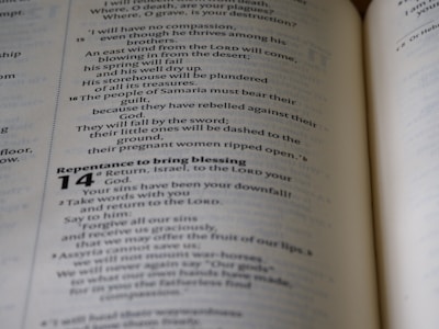 An open book showing text printed in a column format, with headings and verse numbers. The visible page contains religious or biblical content with passages discussing themes such as compassion and repentance.
