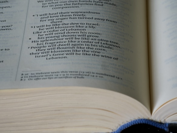 A close-up of an open book with text focused on a passage discussing themes of renewal and growth, using metaphors like dew, lily, cedar, and vine.