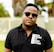 A person is wearing a black polo shirt with text saying 'New Breed of Deep House' and sunglasses. The background shows a blurred outdoor setting with trees and a fence.