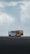 A tour bus with the text 'The Plane Wreck Shuttle' is parked on a desolate and rocky landscape. The sky is overcast with thick clouds, giving the scene a moody atmosphere.