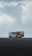 A tour bus with the text 'The Plane Wreck Shuttle' is parked on a desolate and rocky landscape. The sky is overcast with thick clouds, giving the scene a moody atmosphere.