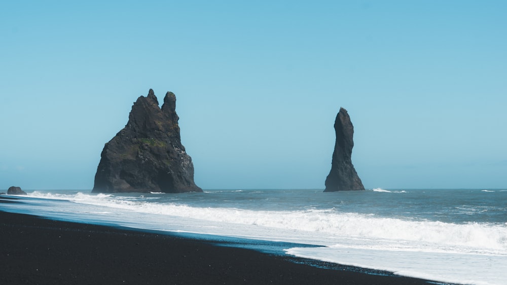 a black sand beach with two large rocks sticking out of the water