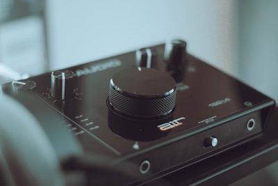The image features an audio interface with a prominent central volume knob and several smaller knobs and switches. The device has a sleek, modern design with branding and labels visible on its surface. The background is softly blurred, highlighting the focus on the audio equipment.