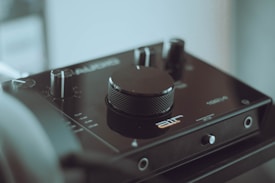 The image features an audio interface with a prominent central volume knob and several smaller knobs and switches. The device has a sleek, modern design with branding and labels visible on its surface. The background is softly blurred, highlighting the focus on the audio equipment.
