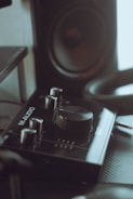 A close-up view of an audio interface with various controls and dials, labeled 'M-Audio', placed next to a speaker. The setup appears to be part of a music production or recording equipment.