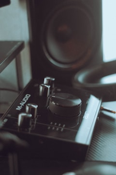 A close-up view of an audio interface with various controls and dials, labeled 'M-Audio', placed next to a speaker. The setup appears to be part of a music production or recording equipment.