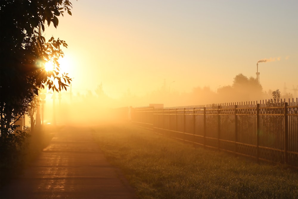 the sun is setting behind a fence on a foggy day