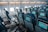 An interior view of an airplane cabin showcasing rows of empty seats equipped with individual screens on the back of each seat. The cabin is well-lit by natural light coming through the airplane windows, highlighting the blue and gray color scheme of the seats.