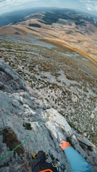 Climber ascending a rocky cliff with a panoramic mountain view.