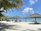 Tourists relaxing at a beach club with tropical drinks and ocean views under a bright sunny sky.