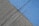 A concrete surface is painted with diagonal lines, featuring a section in blue and another in gray. The texture is rough, with visible grooves and small debris scattered on the surface.
