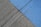 A concrete surface is painted with diagonal lines, featuring a section in blue and another in gray. The texture is rough, with visible grooves and small debris scattered on the surface.