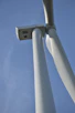 Close-up of wind turbines spinning against a clear blue sky with a technician performing maintenance.