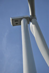 Close-up of wind turbines spinning against a clear blue sky with a technician performing maintenance.