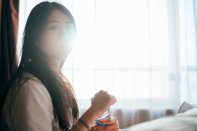 A serene woman sitting peacefully by a window, sunlight softly illuminating her calm face.