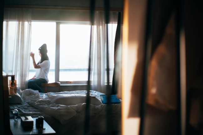 A professional cleaner tidying a spacious, sunlit bedroom.