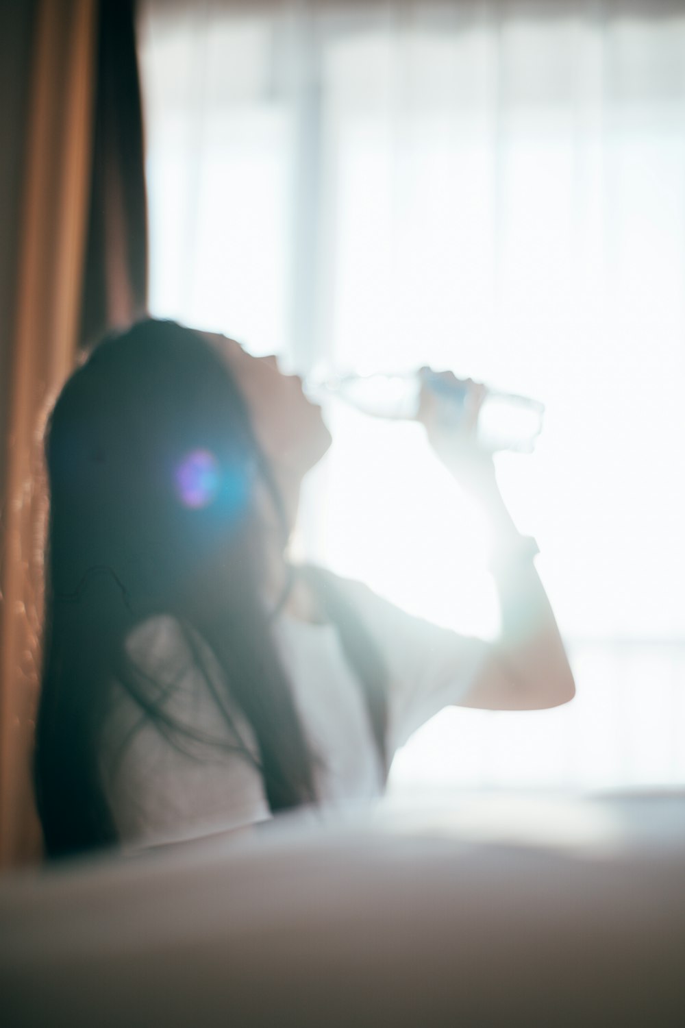 a woman drinking water from a bottle while sitting on a bed