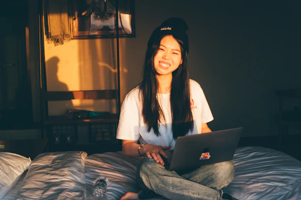 Smiling woman sitting comfortably with a laptop in a warm, sunlit room.