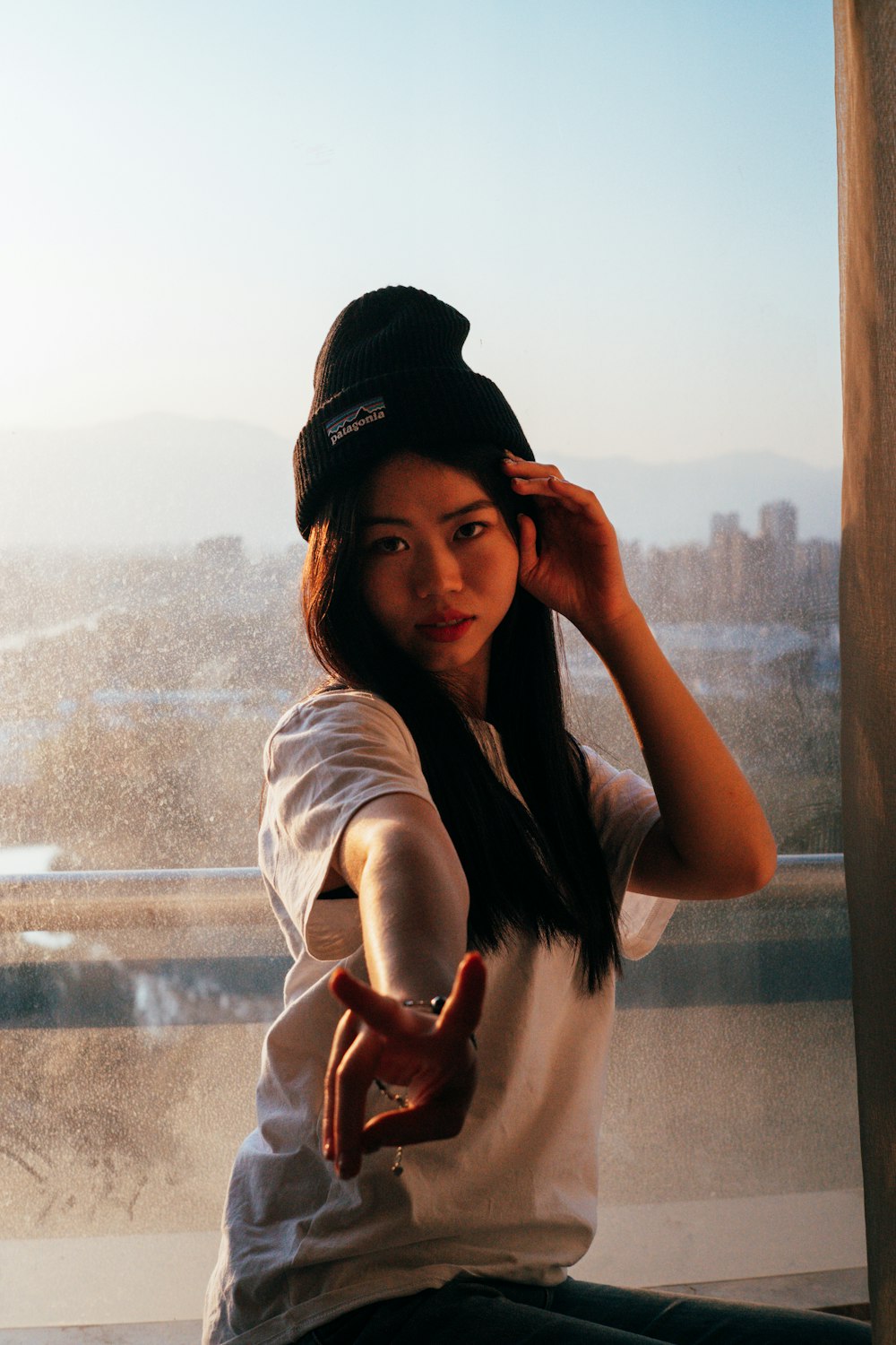 a woman sitting on a window sill wearing a hat