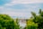 A picturesque view of a bridge under construction over a river, surrounded by lush green trees. The crane in the middle is prominently standing against a backdrop of distant mountains and a cloudy sky.