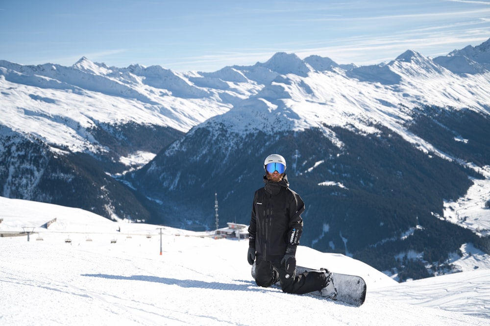a snowboarder sitting on a snowy mountain with mountains in the background