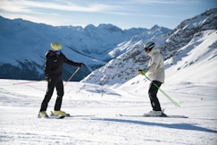 a couple of people riding skis on top of a snow covered slope