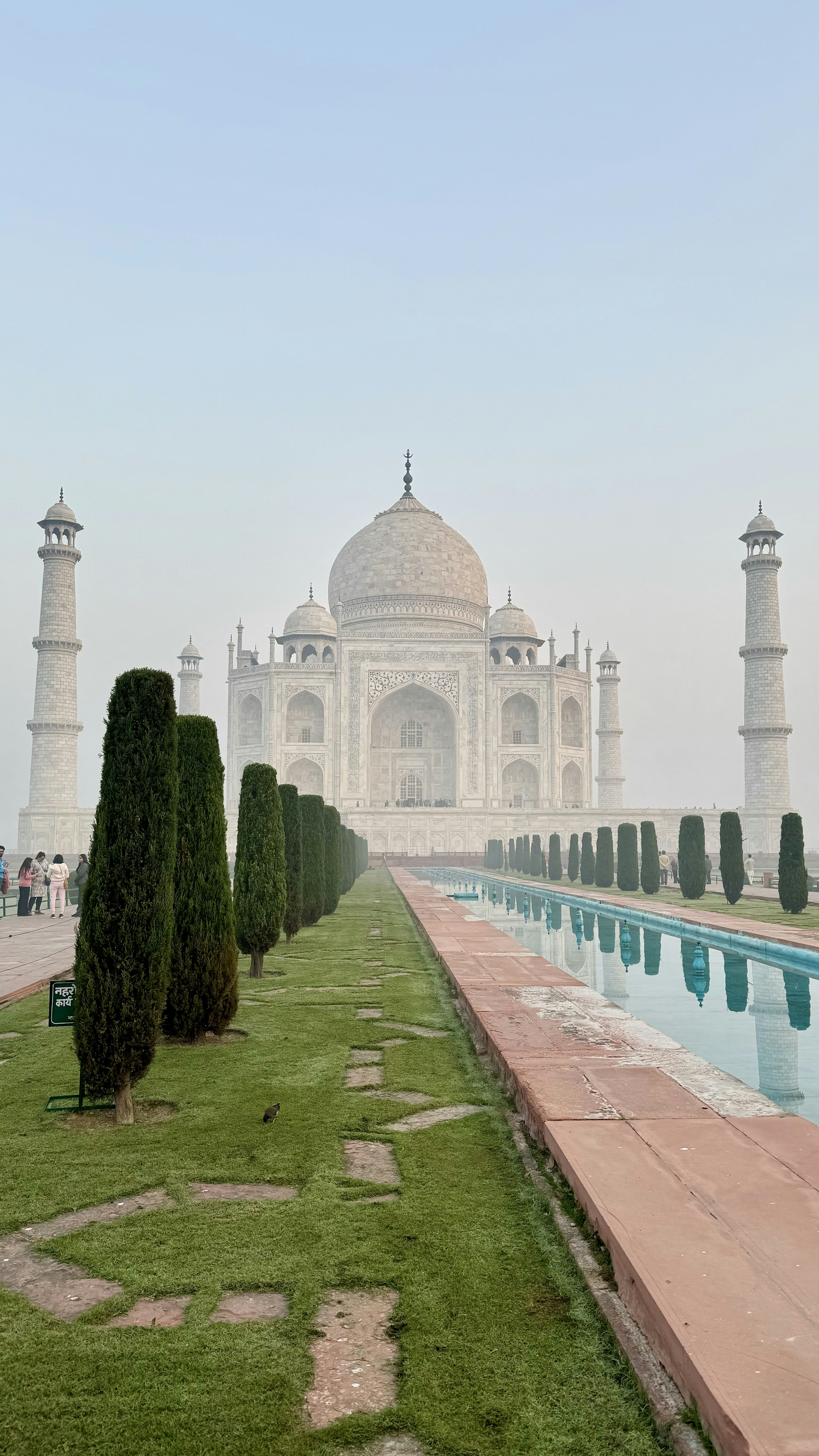 Taj Mahal reflected in long pool at dawn, misty golden morning light, symmetrical marble architecture, soft warm haze