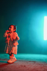 A beautifully styled toddler wearing a dark green velvet dress with gold accents, standing in a softly lit room.