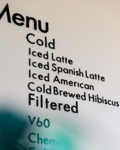A partial view of a cafe menu displaying various cold and filtered beverage options, including types of lattes, cold brews, and filtering methods.