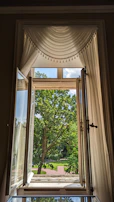 Soft linen curtains gently flowing by a window with a view of a peaceful garden.