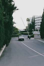 A security patrol vehicle driving along a gated residential estate road lined with trees under a clear sky.